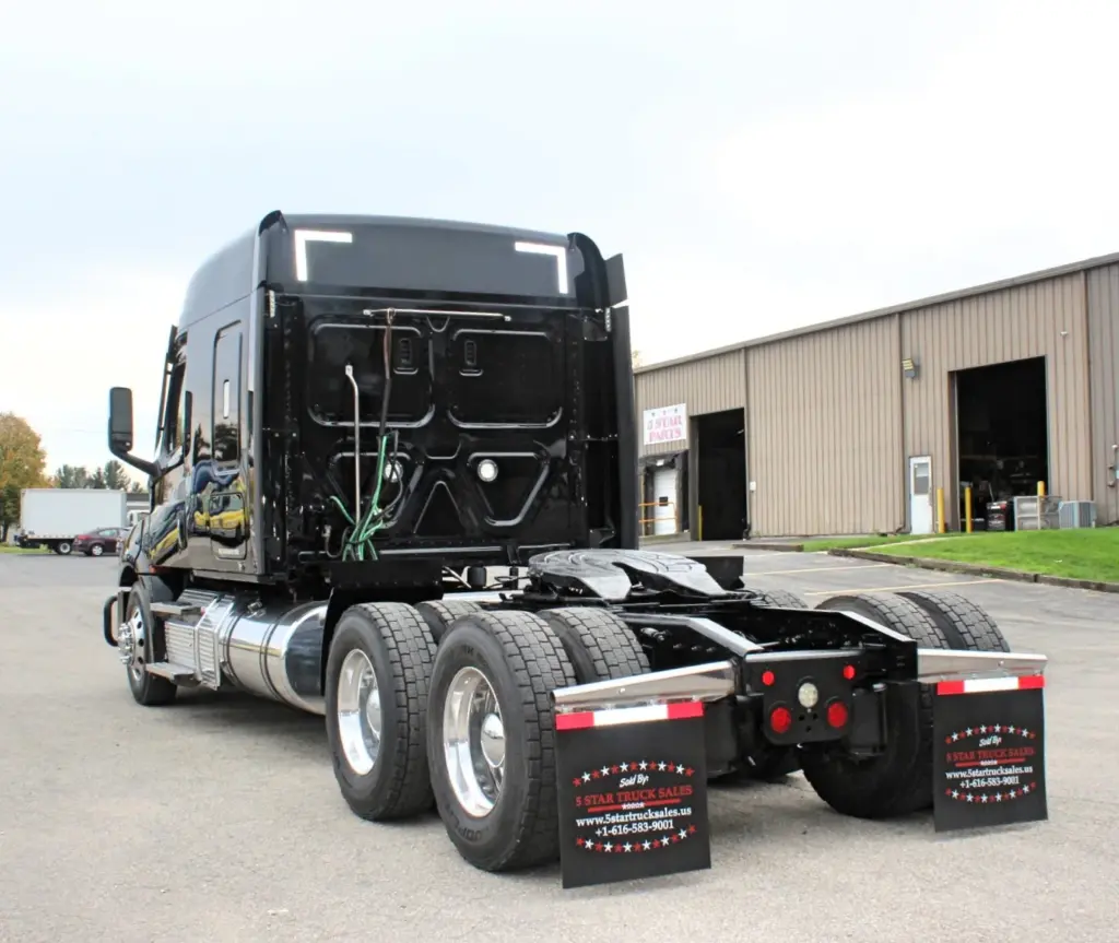 2021 Freightliner Cascadia 126 — angled rear view of black sleeper with polished aluminum tandem wheels and mud flaps.