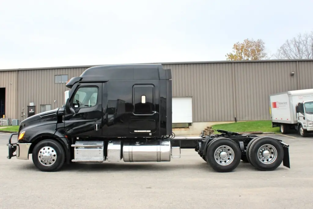 2021 Freightliner Cascadia 126 — full side view of black sleeper tractor with polished aluminum wheels and chrome tanks.