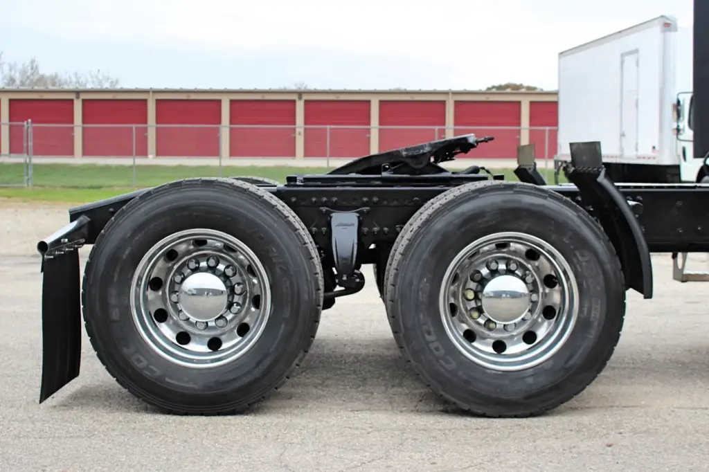 2021 Freightliner Cascadia 126 — close side view of rear tandem wheels, aluminum rims and black suspension.