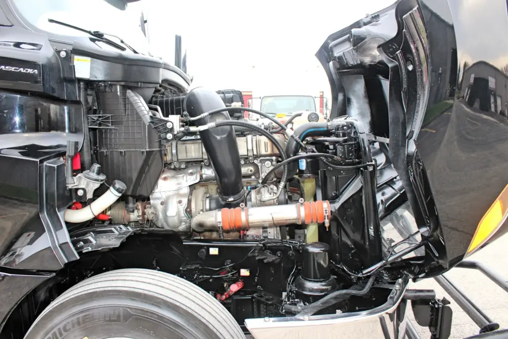 2021 Freightliner Cascadia 126 — open hood view of the black DD15 engine with intake piping and orange charge air couplings.