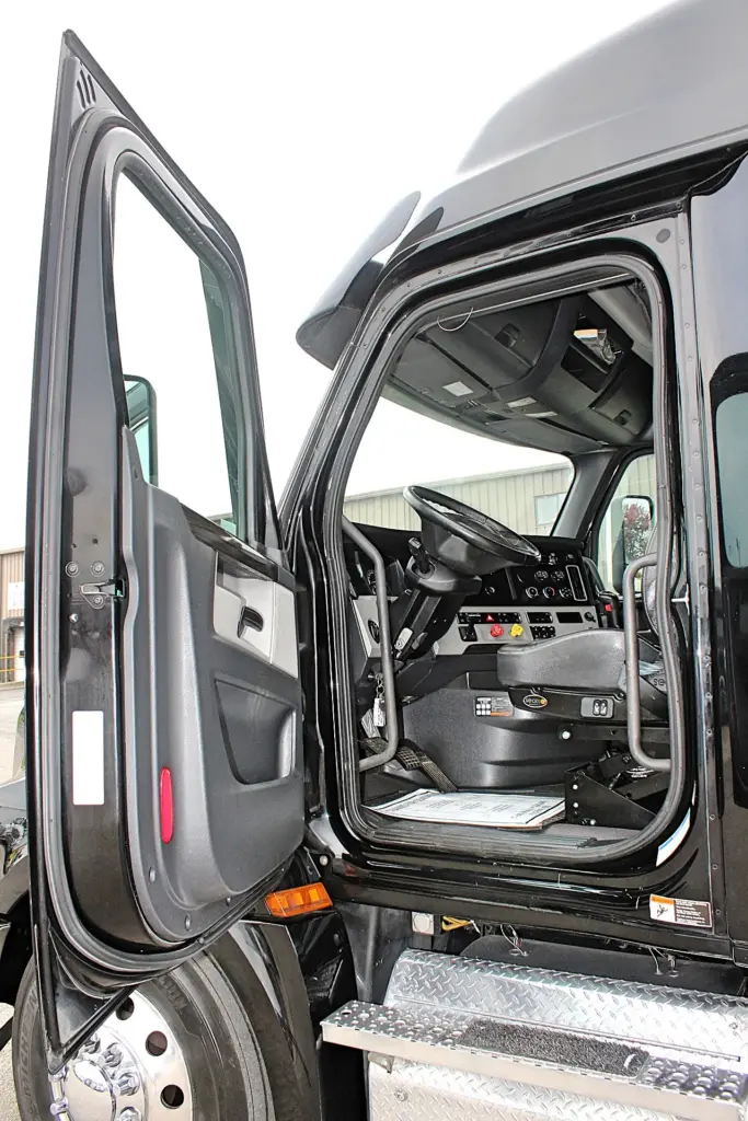 2021 Freightliner Cascadia 126 — open driver door showing steering wheel, dash gauges and gray seat inside cab.