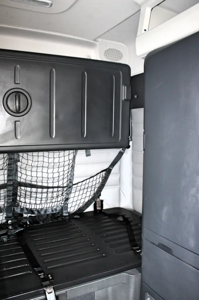 2021 Freightliner Cascadia 126 — angled view of sleeper bunk with black cargo netting and an overhead storage cabinet.