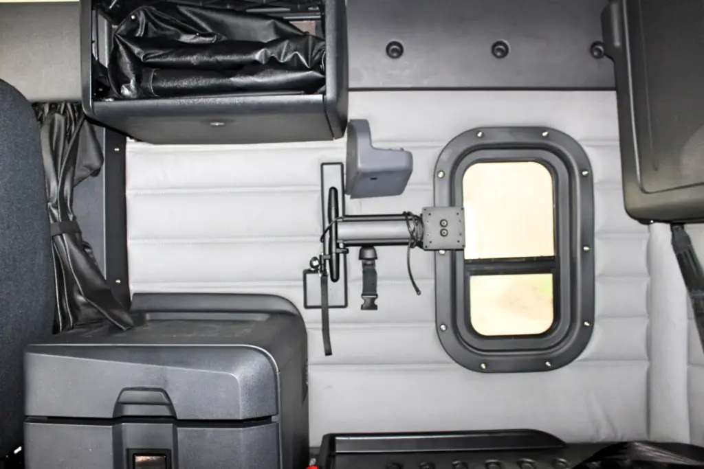 2021 Freightliner Cascadia 126 — wide view of gray sleeper wall, round window and black mounted arm bracket