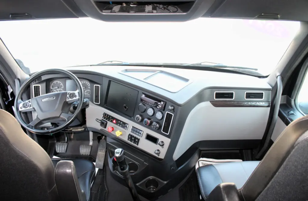2021 Freightliner Cascadia 126 — wide view across cab dash with steering wheel, radio panel and gear shifter visible.